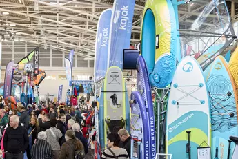 Messestand auf der Messe f.re.e mit bunten SUP-Boards, Kajaks und Wassersportzubehör, umgeben von vielen Besuchern.