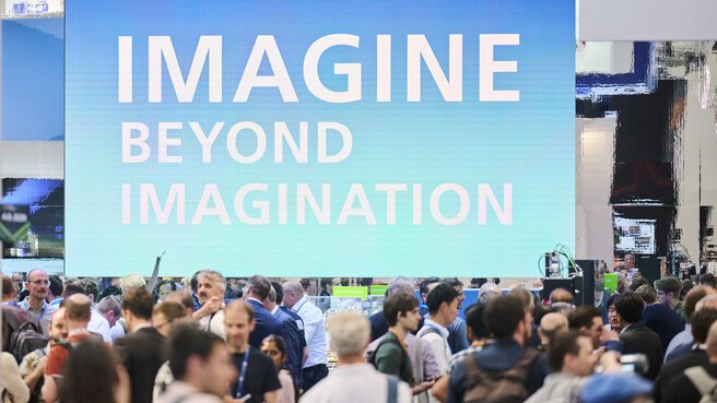 Besuchende vor großem LED-Screen mit der Aufschrift „IMAGINE BEYOND IMAGINATION“ auf der Laser World of Photonics 2025.