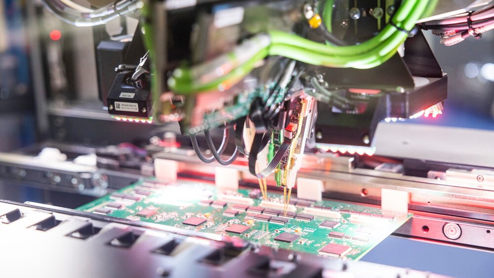 Die Nahaufnahme einer Leiterplatte, die in eine Maschine mit Präzessionswerkzeugen eingespannt ist und bearbeitet wird.