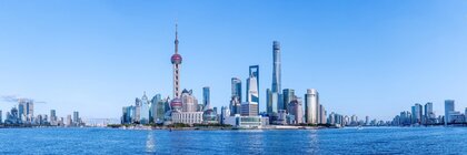 Die Wolkenkratzer-Skyline von Shanghai, davor der Huangpu Fluss mit einem fast wolkenlosen blauen Himmel darüber.