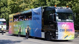 A colorful parade float with “Our Strength” banners and people on board at the 2026 CSD, escorted by staff members.