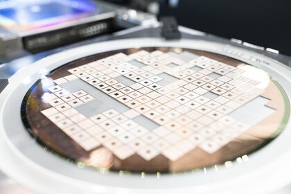 Close-up of a circular wafer in a laboratory or production setup, covered with many square microstructures arranged in a regular grid pattern.