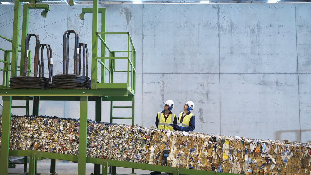 Zwei Arbeiter stehen an einem Förderband in einer Recyclinganlage für Papier
