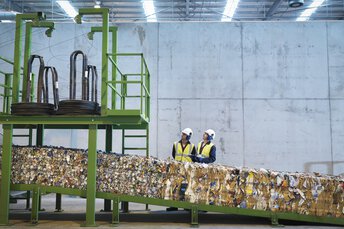  Zwei Arbeiter stehen an einem Förderband in einer Recyclinganlage für Papier