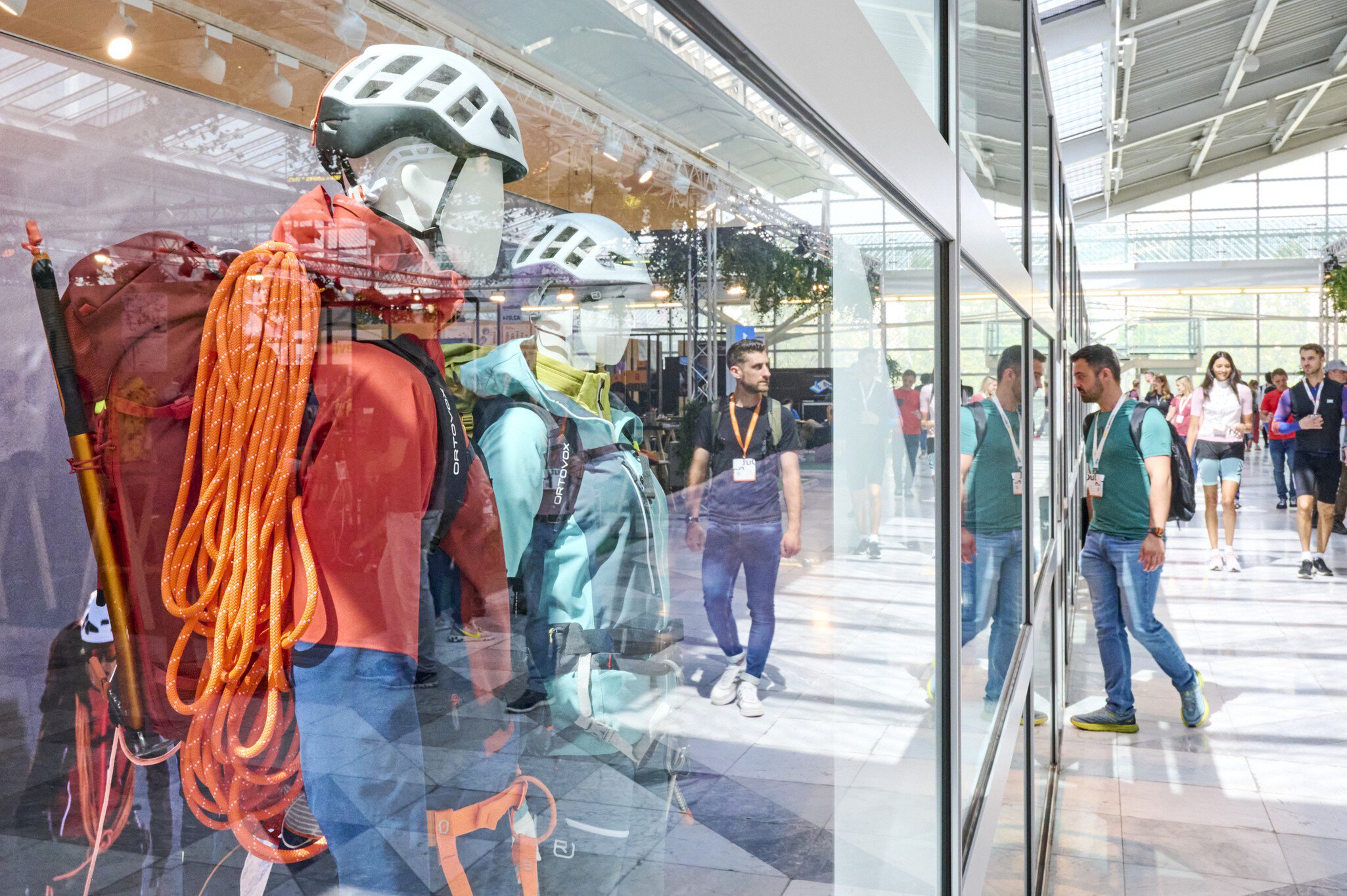 Fachbesucher betrachten im Atrium des MOC Ordercenter zwei Schaufensterpuppen, die mit Outdoor-Funktionskleidung und Sportkletter-Equipment ausgestattet sind.