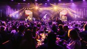A large crowd at the AWARD Gala with purple lighting and stage screens, people sitting at tables.