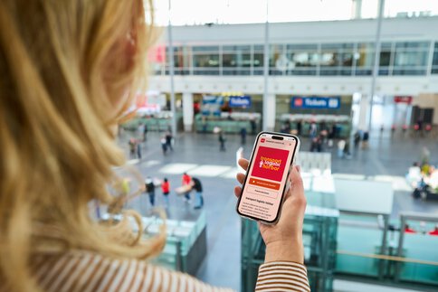 Eine Frau hält ein Smartphone in der Hand, auf dem man den transport logistic Podcast sieht.