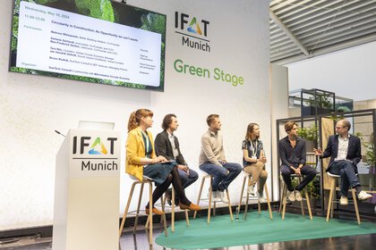 Panel discussion at IFAT Munich, Green Stage, with six people and a large screen with event branding.