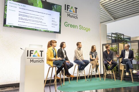 Podiumsdiskussion auf der IFAT Munich, Green Stage, mit sechs Personen und einer großen Leinwand mit Event-Branding.