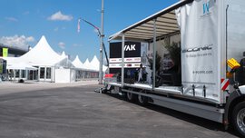 Offener Trailer-Messestand von VAK auf der IFAT Munich mit Branding ‚e-Econic – In charge for a new era‘, Sitzbereich und weißen Zelten im Hintergrund unter blauem Himmel.