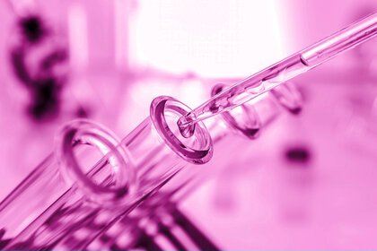 Close-up of a pipette filled with liquid dripping into a test tube, held in a light violet tone.
