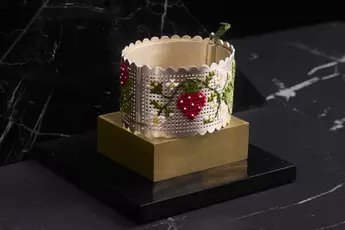 Geprägtes Silberarmband mit rotem Beeren- und grünem Blättermuster, präsentiert auf einem schwarz-goldenen Ständer.