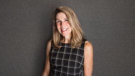 Eine lächelnde Frau mit langen blonden Haaren in einem schwarz und weiß karierten schulterfreien Kleid.