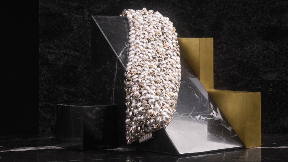 Bracelet with metallic embellishments on a black and gold geometric structure against a dark marble background.