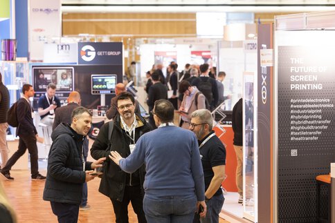 People talking in a busy LOPEC exhibition hall with various stands and signage in the background.