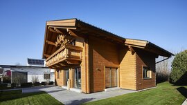 Ein Holzhaus im Chalet-Stil mit schrägem Dach, umgeben von grünem Gras und einem klaren blauen Himmel.