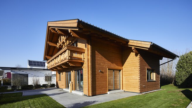 Ein Holzhaus im Chalet-Stil mit schrägem Dach, umgeben von grünem Gras und einem klaren blauen Himmel.