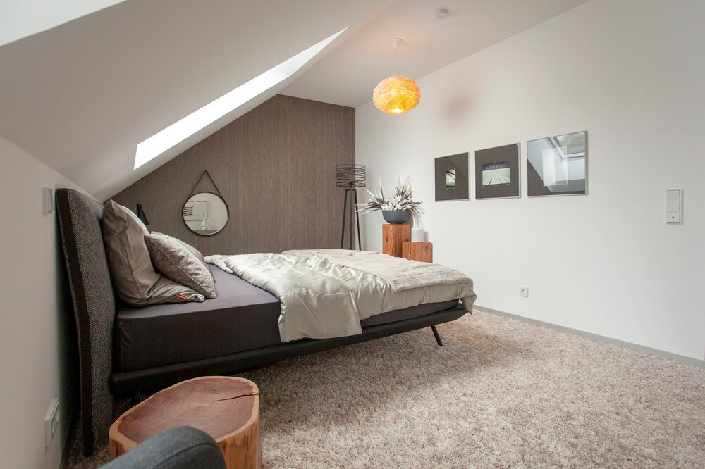 Modernes Dachgeschossschlafzimmer mit Dachschräge, Doppelbett, Kunstwerken an den Wänden und einem kleinen Nachttisch aus Holz mit Lampe.