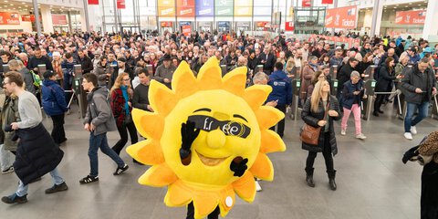 Das Maskottchen der f.re.e, eine gelbe Sonne mit Sonnenbrille, steht im Eingangsbereich der Messe und posiert vor den Besuchern an den Ticketkontrollen.