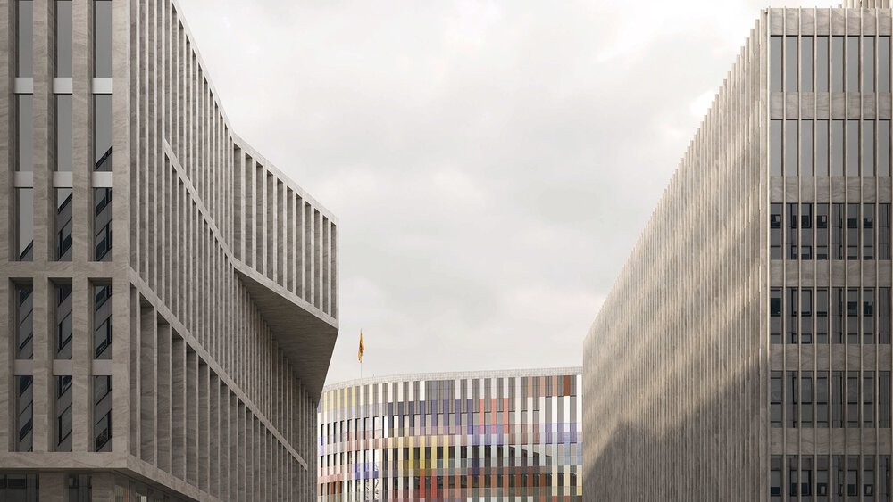 Ein modernes Gebäude mit bunter Fassade am Ende einer Straße. Im Vordergrund erheben sich rechts und links graue Gebäudekomplexe.
