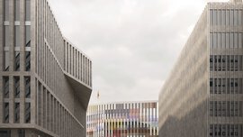 Ein modernes Gebäude mit bunter Fassade am Ende einer Straße. Im Vordergrund erheben sich rechts und links graue Gebäudekomplexe.