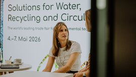 Gespräch am Stand der IFAT Munich auf dem SZ Nachhaltigkeitsgipfel 2025 vor einer Infowand zur Messe. 