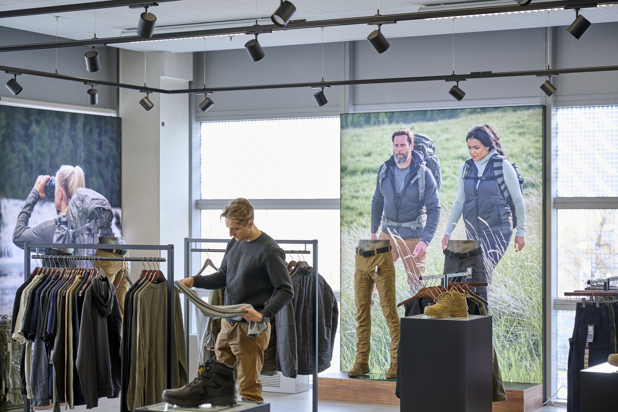 Eine Person untersucht ein Kleidungsstück auf der Ausstellungsfläche des MOC Ordercenters. Im Hintergrund sieht man große Bilder von sportlichen Menschen in der Natur.