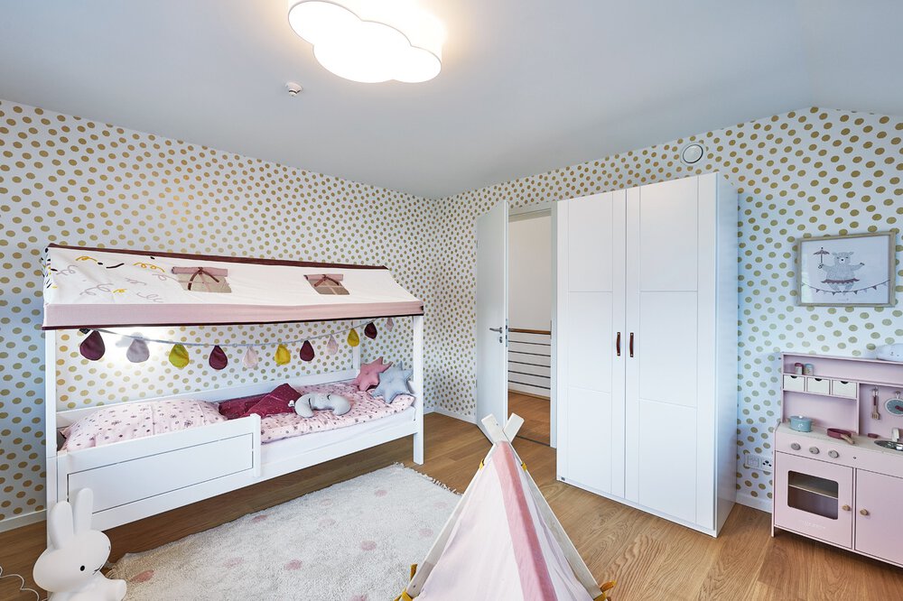 Kinderzimmer mit Bett, gemusterter Tapete, weißem Kleiderschrank und Spielzelt auf Holzboden.