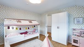 Kinderzimmer mit Bett, gemusterter Tapete, weißem Kleiderschrank und Spielzelt auf Holzboden.