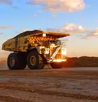 A large dump truck drives along a dirt road at sunset.