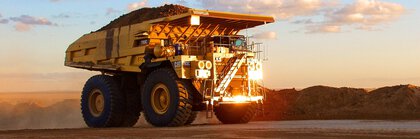 A large dump truck drives along a dirt road at sunset.
