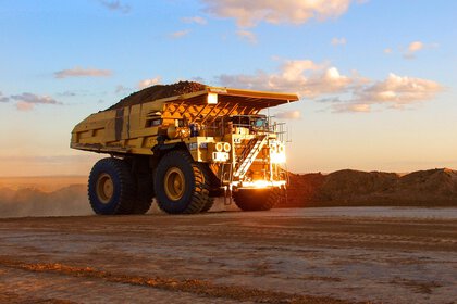 A large dump truck drives along a dirt road at sunset.