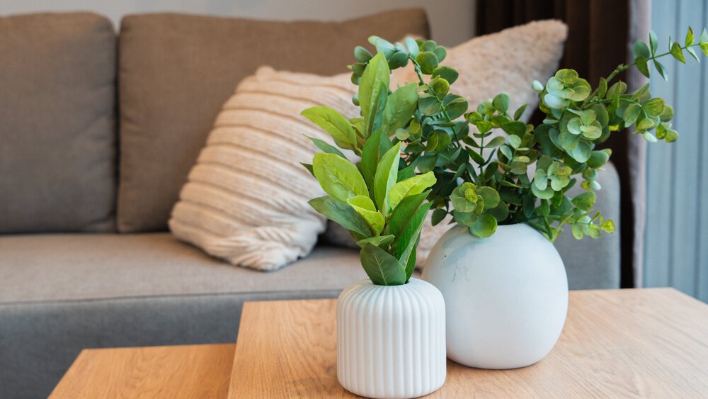 Nahansicht eines hölzernen Couchtischs mit zwei weißen Vasen und einem grauen Sofa  mit weißen Kissen dahinter.