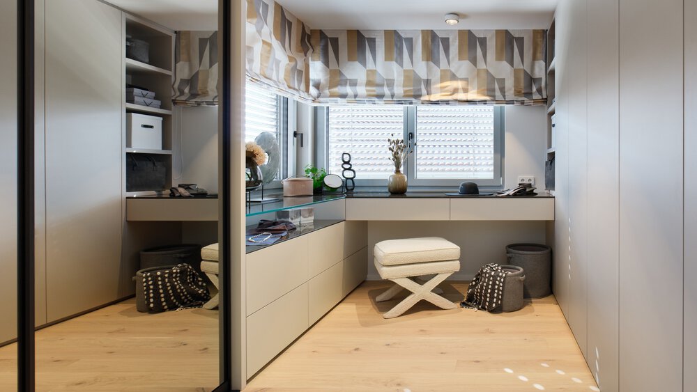 Modernes Ankleidezimmer mit Spiegelwand, Frisiertisch, geometrischen Vorhängen und gepolstertem Hocker auf Holzboden.