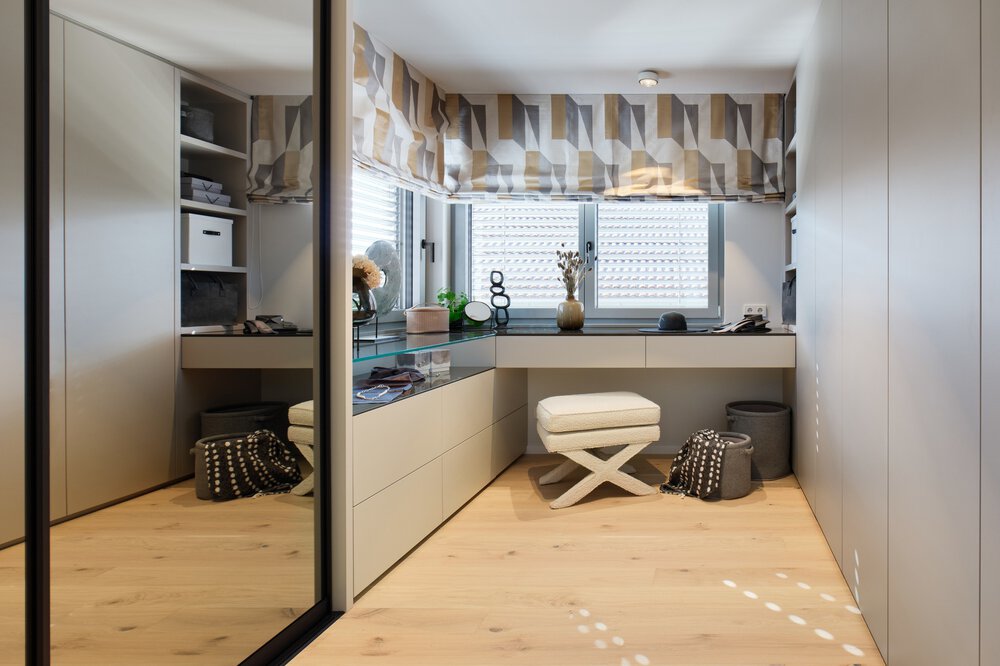 Modernes Ankleidezimmer mit Spiegelwand, Frisiertisch, geometrischen Vorhängen und gepolstertem Hocker auf Holzboden.