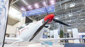 Ein weiß-rotes leichtes Propellerflugzeug steht in einer Halle der productronica unter dem Schild „Innovation and leading technology made in Europe“.