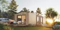 Moderne Holzhütte mit großen Fenstern, umgeben von Bäumen und Gras, bei Sonnenuntergang. Auf dem Rasen sitzt ein kleiner Hase.
