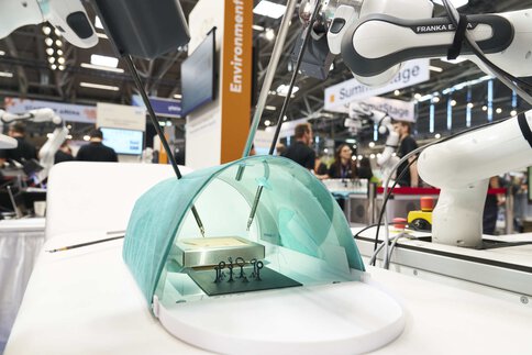 Robotic arm performs medical simulation with instruments under green cover.