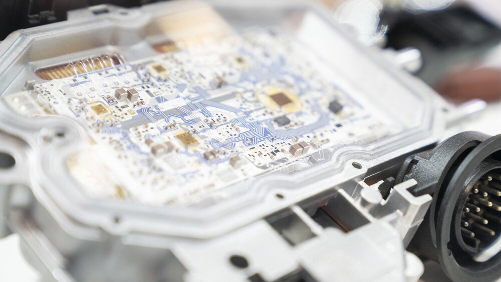 Nahansicht einer weißen und blauen Leiterplatine, die in einem geöffneten Gehäuse an einem Stand der productronica präsentiert wird.