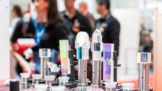 Various glass prisms and optical devices on display at a trade fair stand, people can be seen out of focus in the background.