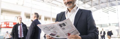 Mann im Anzug lächelt, während er im hellen, geräumigen Eingangsbereich der LOPEC Messe eine Broschüre liest.