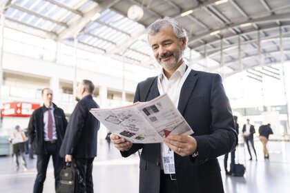 A man in a suit smiles as he reads a brochure in the bright, spacious entrance area of the LOPEC trade fair.