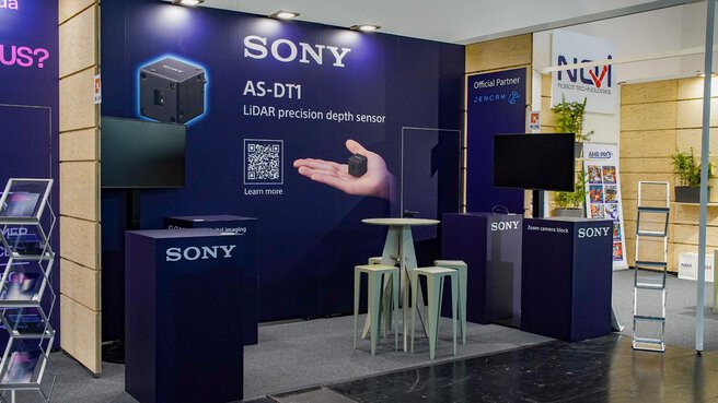 Sony trade fair booth featuring a large banner for the AS-DT1 LiDAR precision depth sensor, QR code, monitors, and seating furniture.