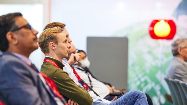 Eine Reihe Zuschauer sitzt auf Stühlen und sieht aufmerksam nach vorne.