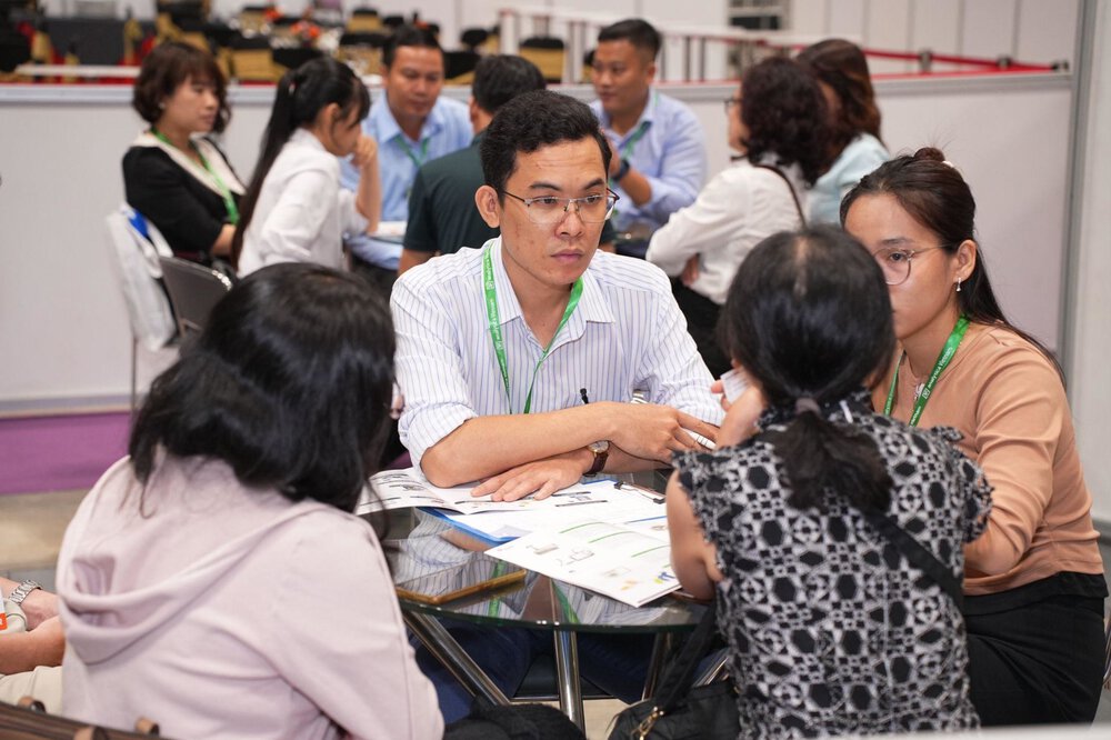 A group of people sit around a table at a professional event or conference and discuss.