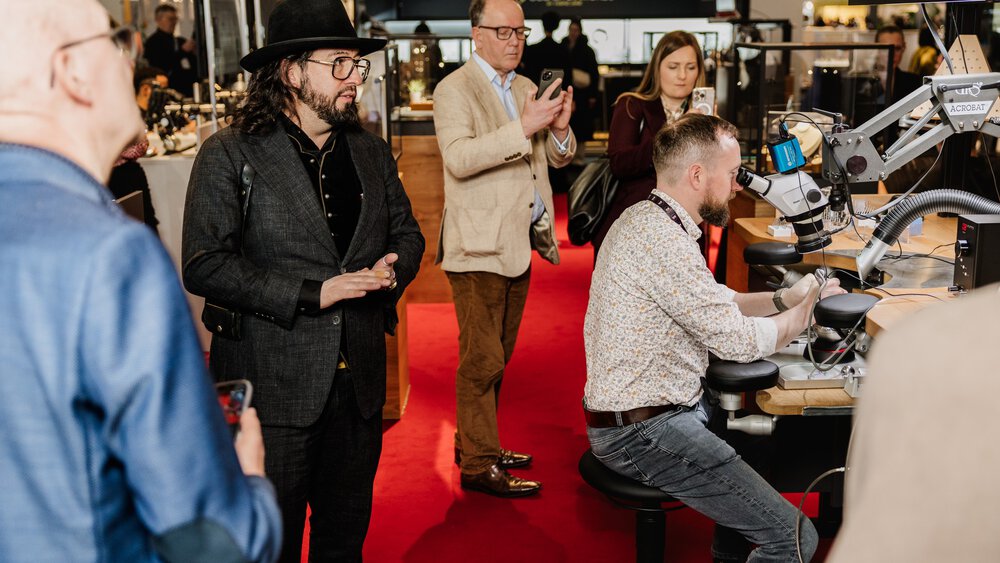 During an event with a red carpet and exhibition stands, visitors watch a craftsman at work in his workplace.