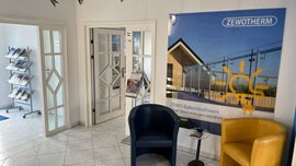 Moderner Büro-Wartebereich mit zwei Stühlen, einem Tisch, Broschüren und einem ZEWO-Poster an der Wand.