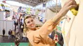 Besucherin erklimmt den Kletterturm der Freizeitmesse f.re.e 2025 und zeigt ihre Kletterfähigkeiten und schaut lächeln in die Kamera.