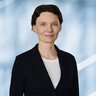 Eine lächelnde Frau mit kurzen Haaren, schwarzem Jackett und weißem Hemd.