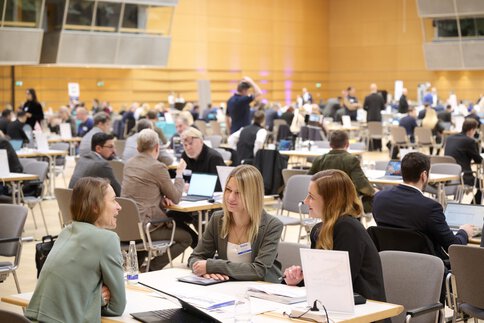 Journalist sitting at a table talking to two exhibitors. You can find tables in similar situations in the background
